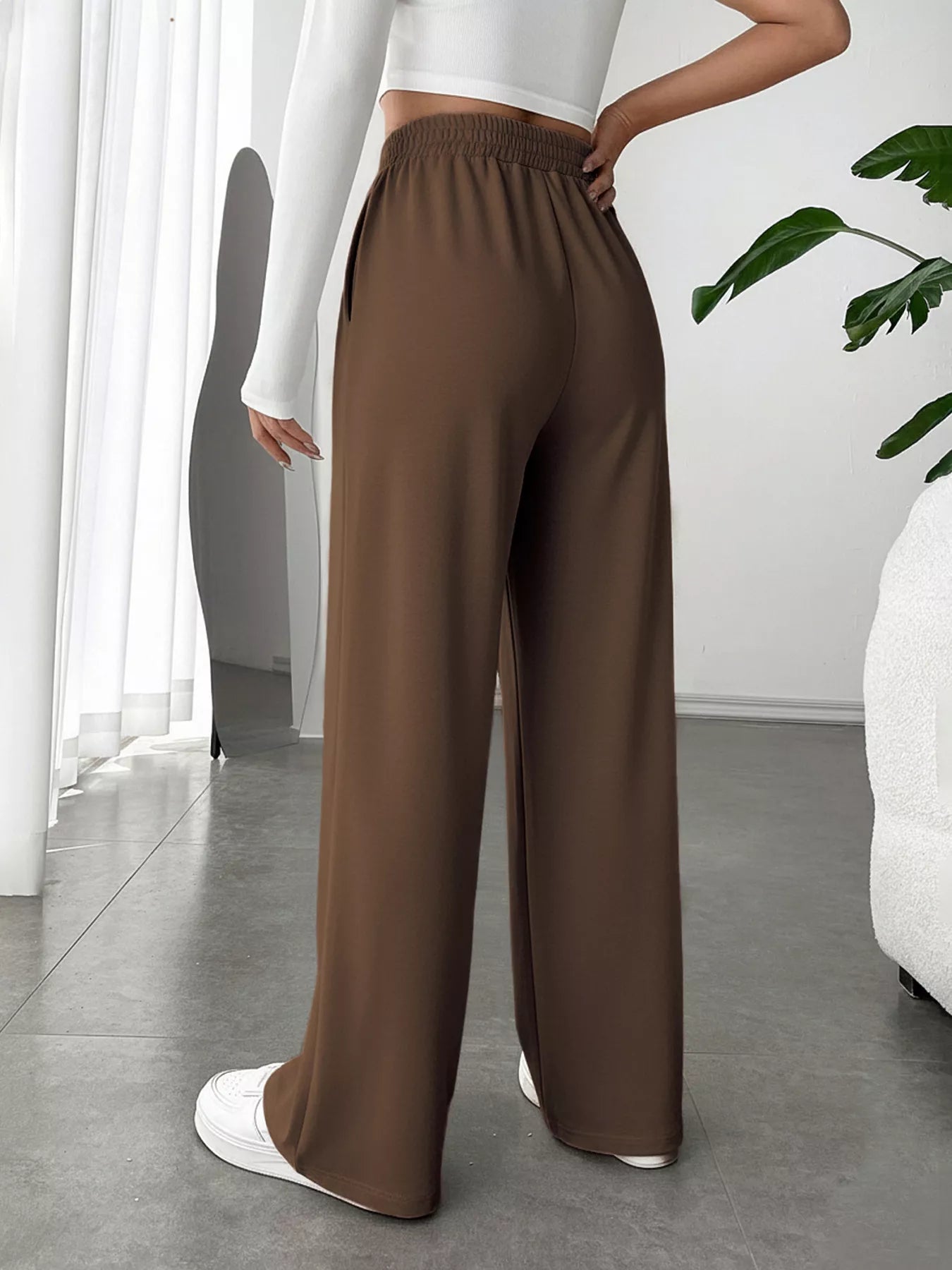 Brown wide-leg pants worn by a person in a minimalistic room.