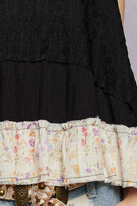 Black layered dress with floral hem and denim jeans on a neutral background