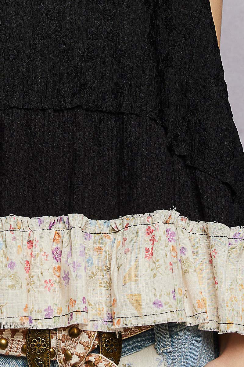 Black layered dress with floral hem and denim jeans on a neutral background