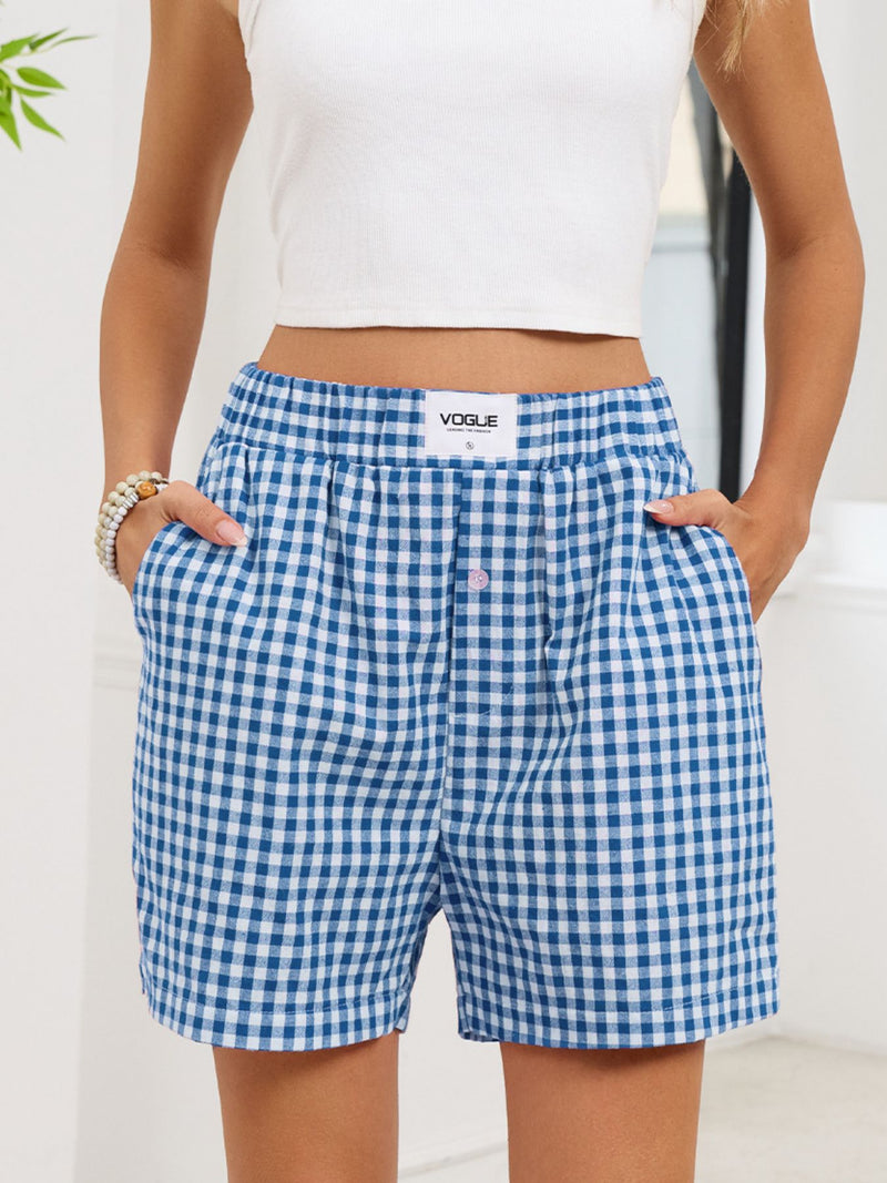 Person wearing blue gingham shorts with a visible 'Vogue' label, standing against a white background.