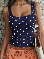 Person wearing a navy blue tank top with white polka dots against a stone wall.