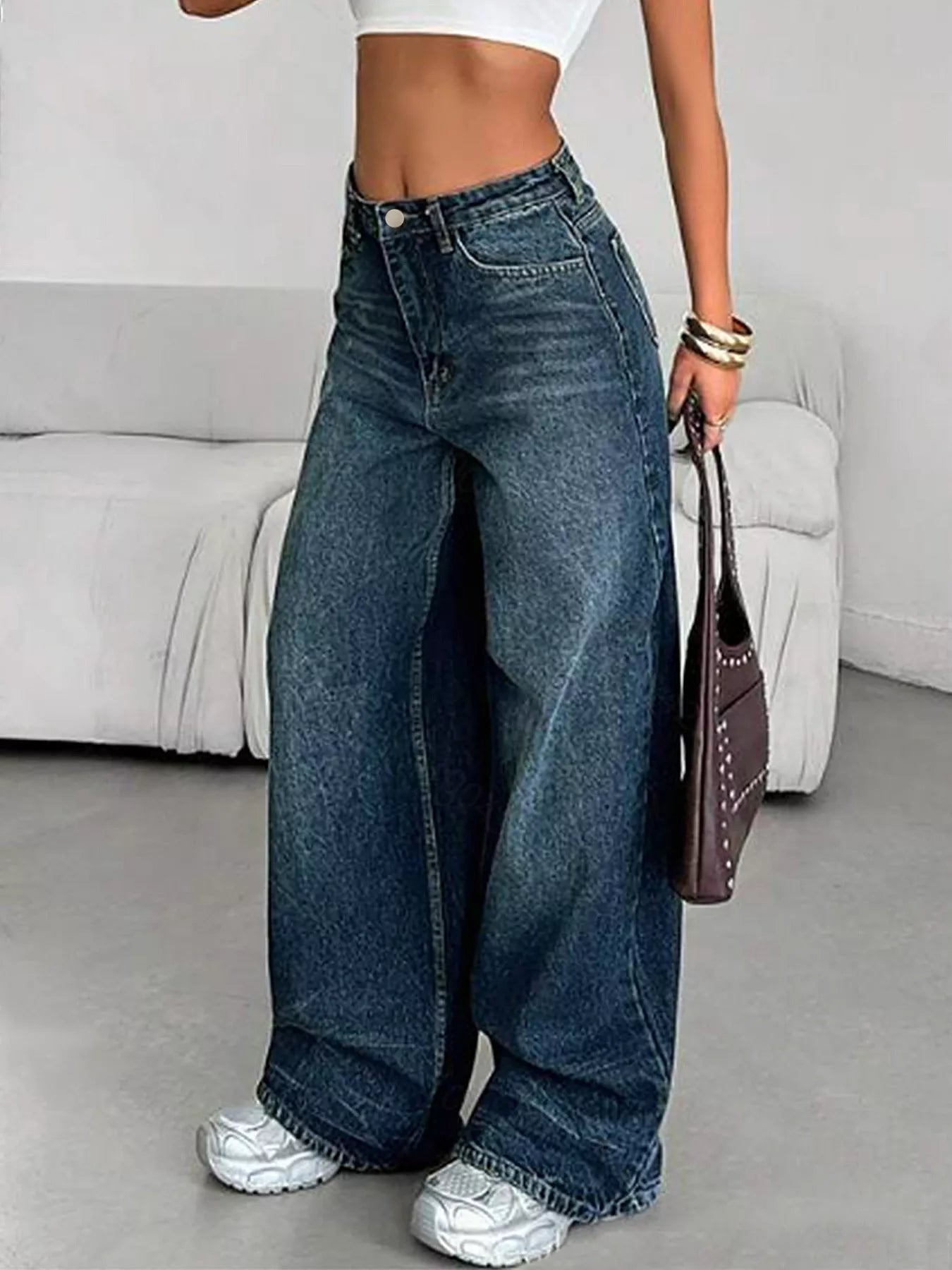 Person wearing wide-leg jeans holding a handbag in a minimalistic room.
