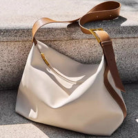 White handbag with brown leather strap on a textured surface