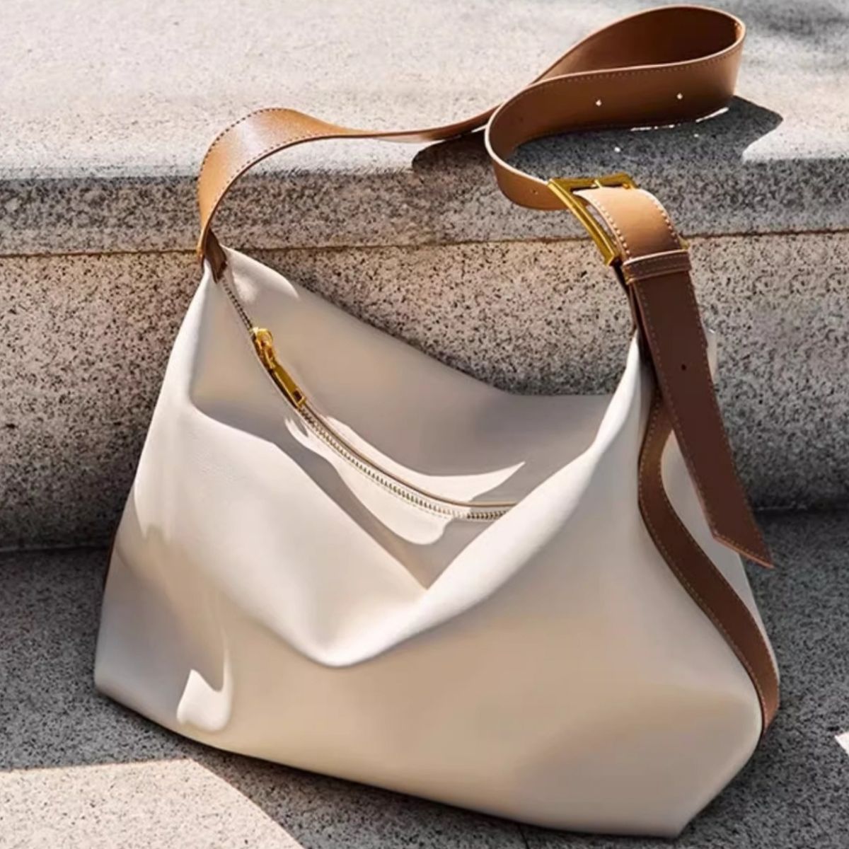 White handbag with brown leather strap on a textured surface