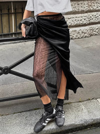Person wearing a black sheer skirt with a white top and black sneakers on a city street.