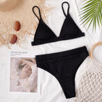 Black bikini set on a textured surface with a magazine and decorative elements.