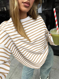 Person wearing a white and brown striped sweater holding a green drink with a straw.
