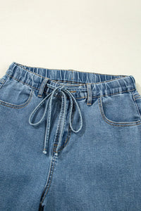 Blue denim paperbag pants with a tie waist on a light background