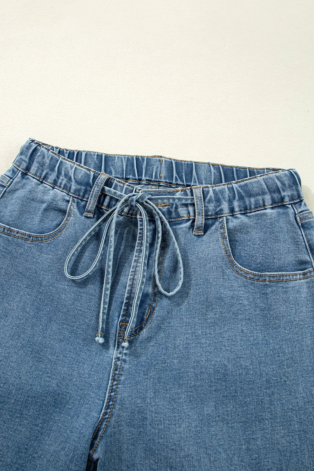 Blue denim paperbag pants with a tie waist on a light background