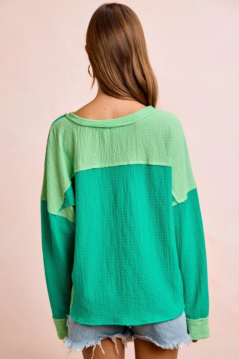 Green and teal color-blocked top worn by a person on a beige background