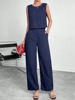 Woman wearing a navy blue sleeveless top and wide-leg pants, holding a red handbag.