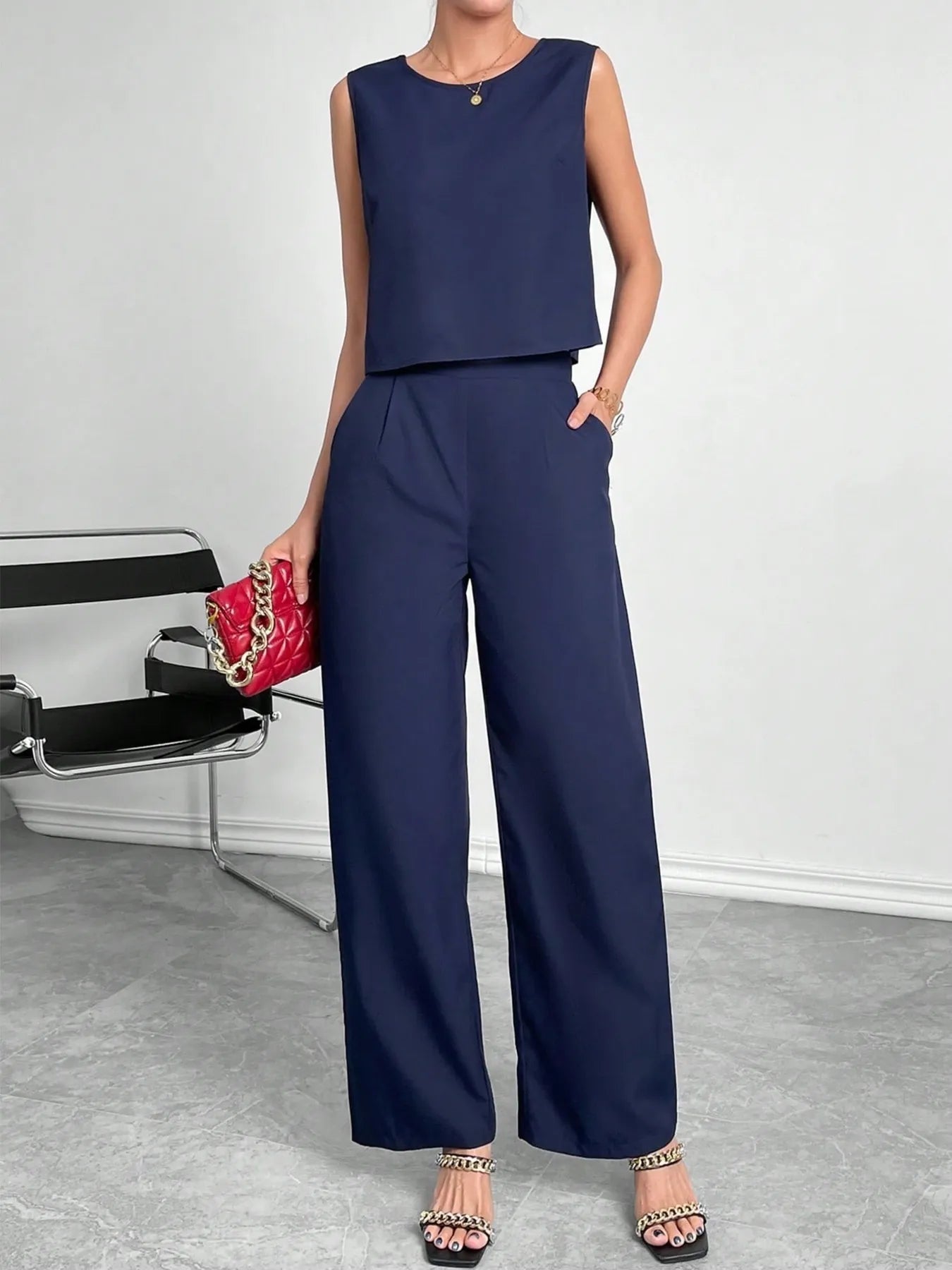 Woman wearing a navy blue sleeveless top and wide-leg pants, holding a red handbag.