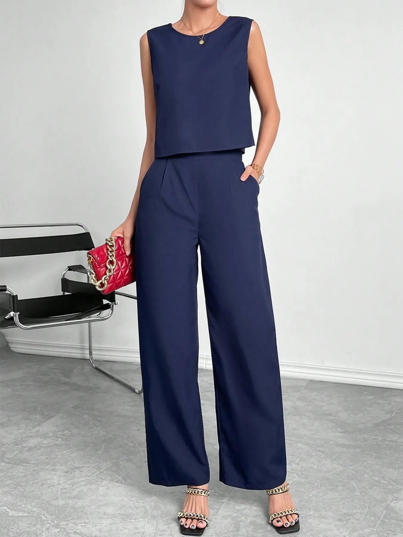 Woman wearing a navy blue sleeveless top and wide-leg pants, holding a red handbag.