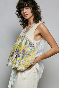 Woman wearing a sleeveless floral top and white pants against a gray background