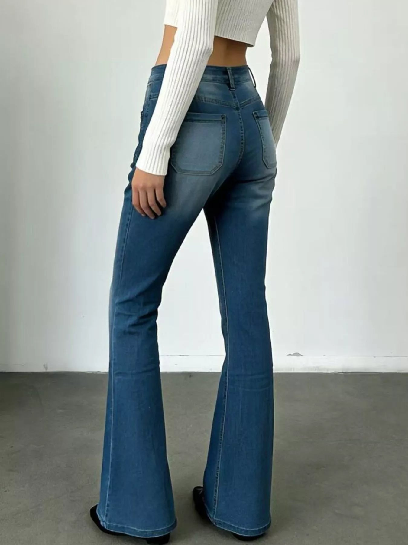 Person wearing blue flared jeans and a white cropped top against a plain background
