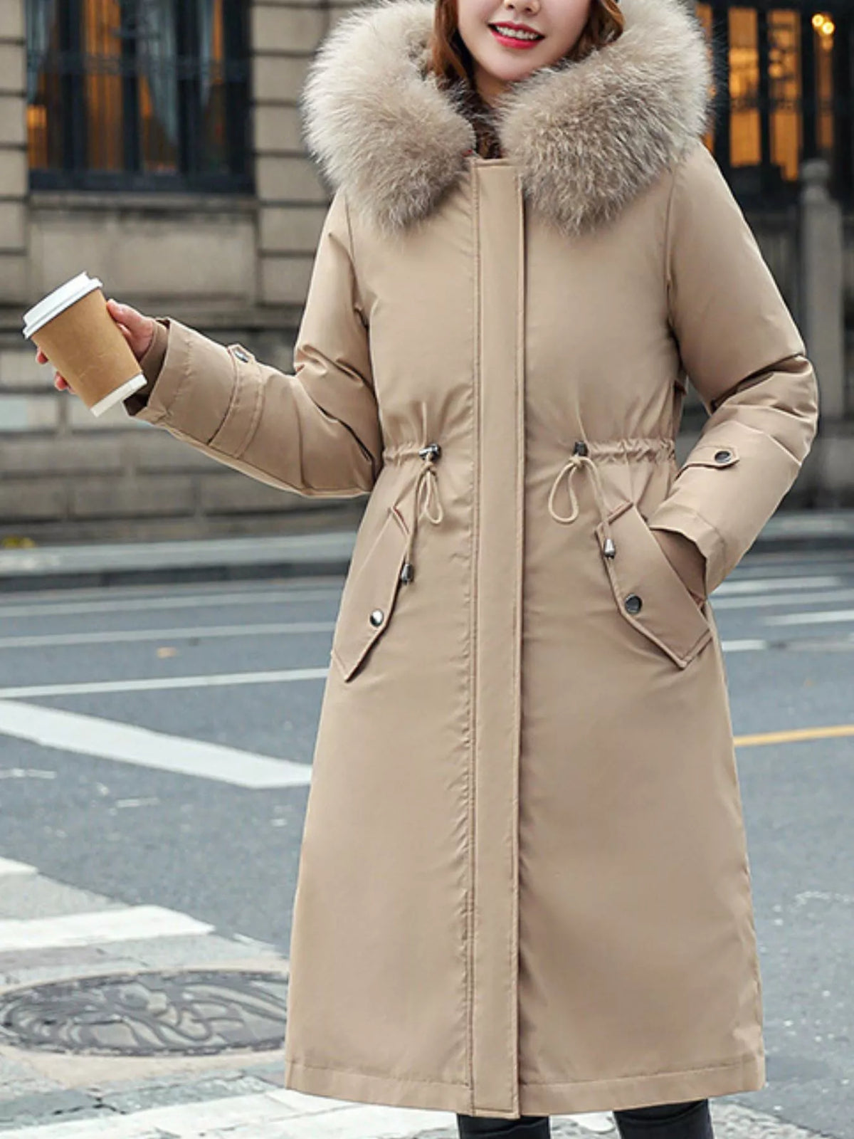 Lady wearing a biege Women's Detachable Longline Hooded Parka with Faux Fur Trim and Drawstring Waist with a coffee cup in her hand
