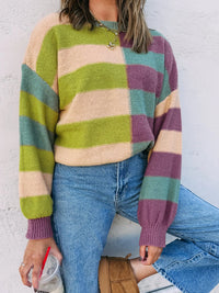 Person wearing a colorful striped sweater and blue jeans against a white wall.