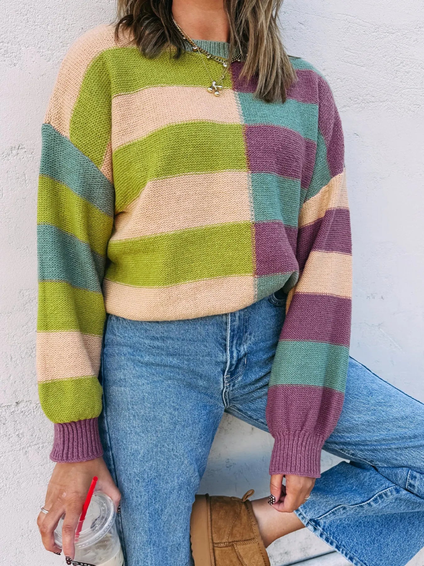 Person wearing a colorful striped sweater and blue jeans against a white wall.