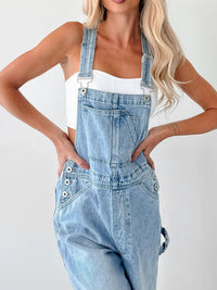 Person wearing light blue denim overalls on a white background