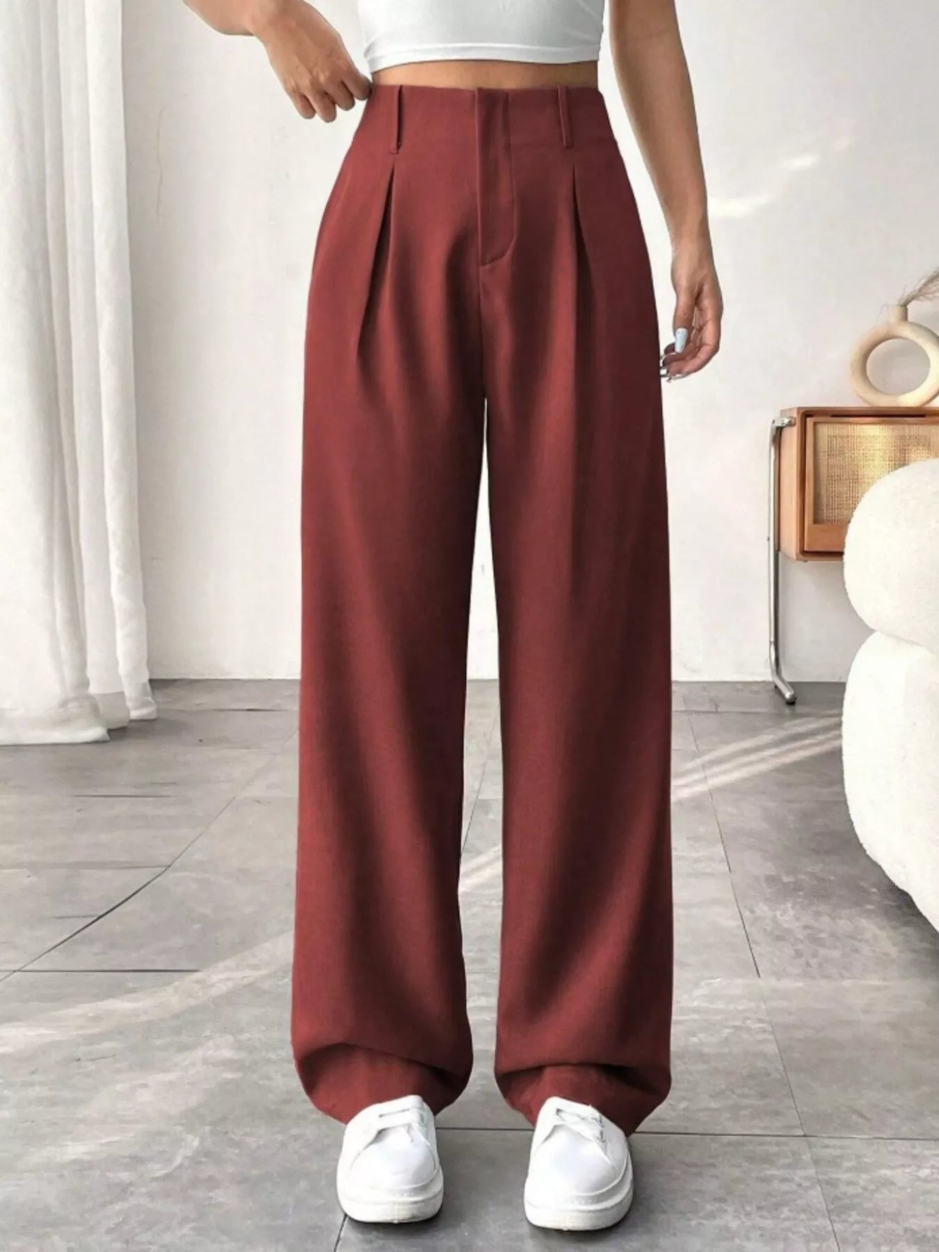 Person wearing maroon wide-leg pants and white sneakers in a minimalistic room.