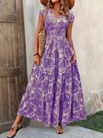 Woman wearing a purple floral dress standing against a wooden door and concrete wall.