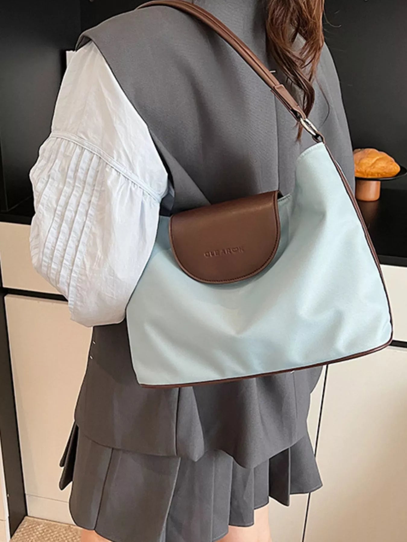 Person wearing a light blue handbag with a brown flap over a dark background