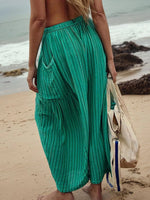 Person wearing teal pants on a beach with a white bag.