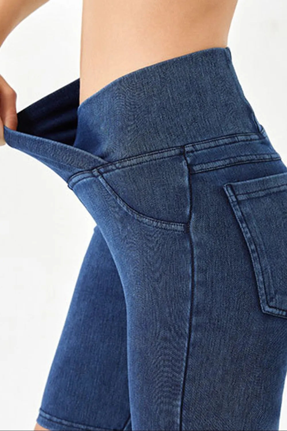 Close-up of blue jeans being pulled up on a person against a white background