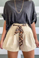 Person wearing a black oversized top and beige shorts with a leopard print belt.
