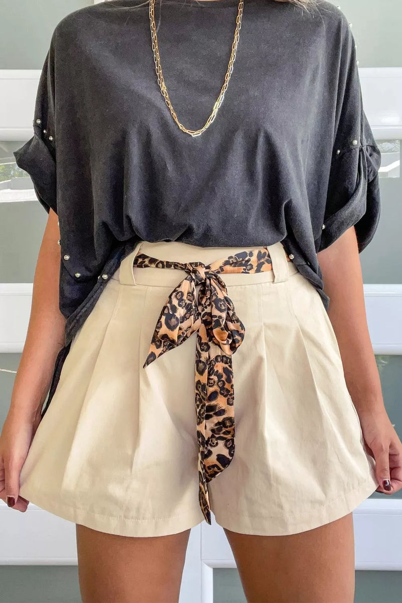 Person wearing a black oversized top and beige shorts with a leopard print belt.