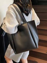 Person holding a black leather tote bag indoors.
