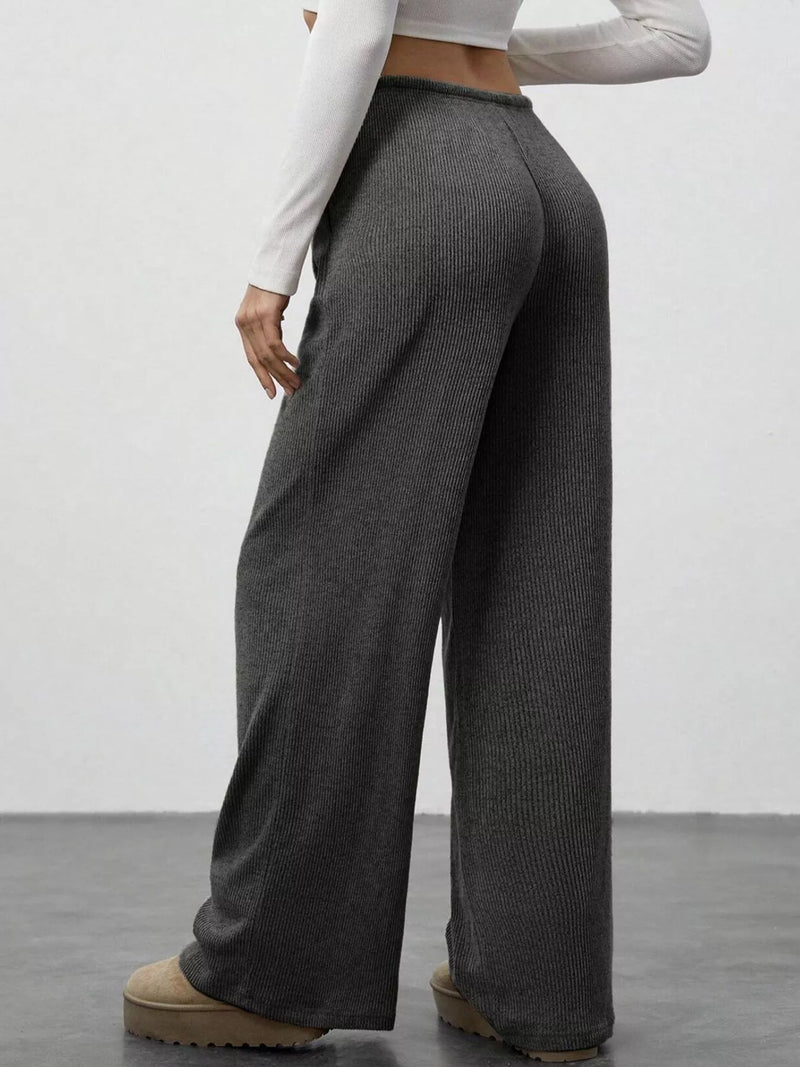 Person wearing gray ribbed wide-leg pants with a white top and brown shoes on a plain background