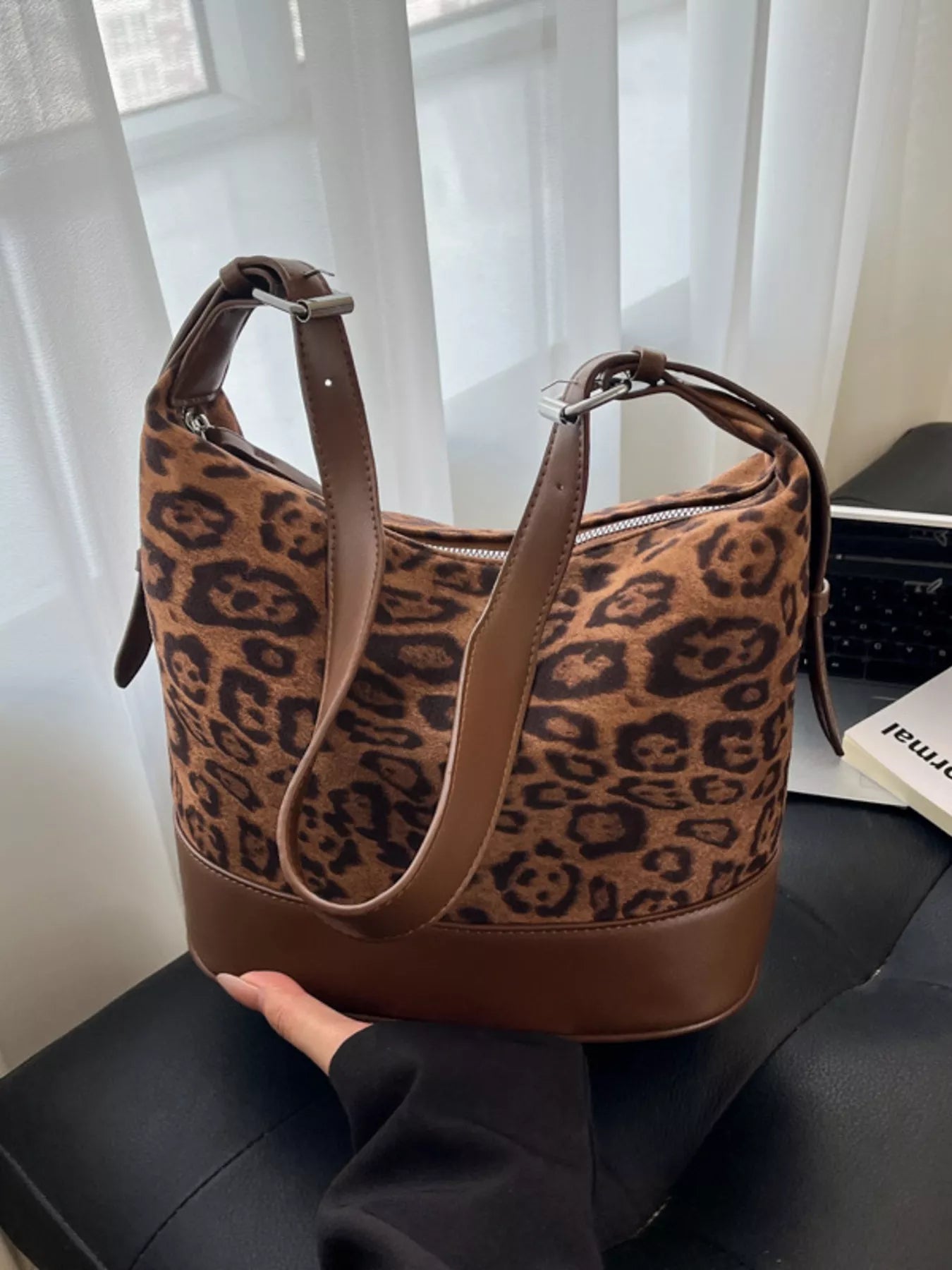 Leopard print handbag with brown leather straps on a black surface.