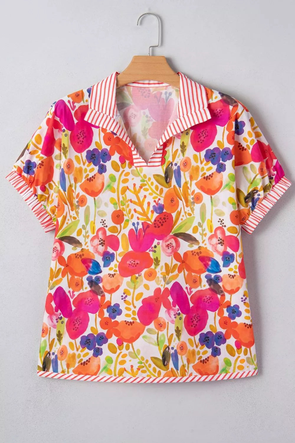 Colorful floral blouse on a hanger against a gray background