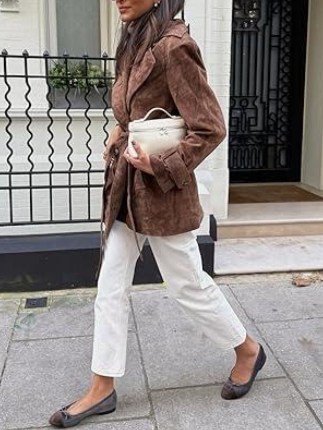 Person wearing a brown coat and white pants walking outdoors.