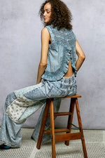 Woman wearing a denim outfit sitting on a wooden stool against a gray wall.