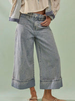 Person wearing wide-leg jeans and a striped shirt on a light green background
