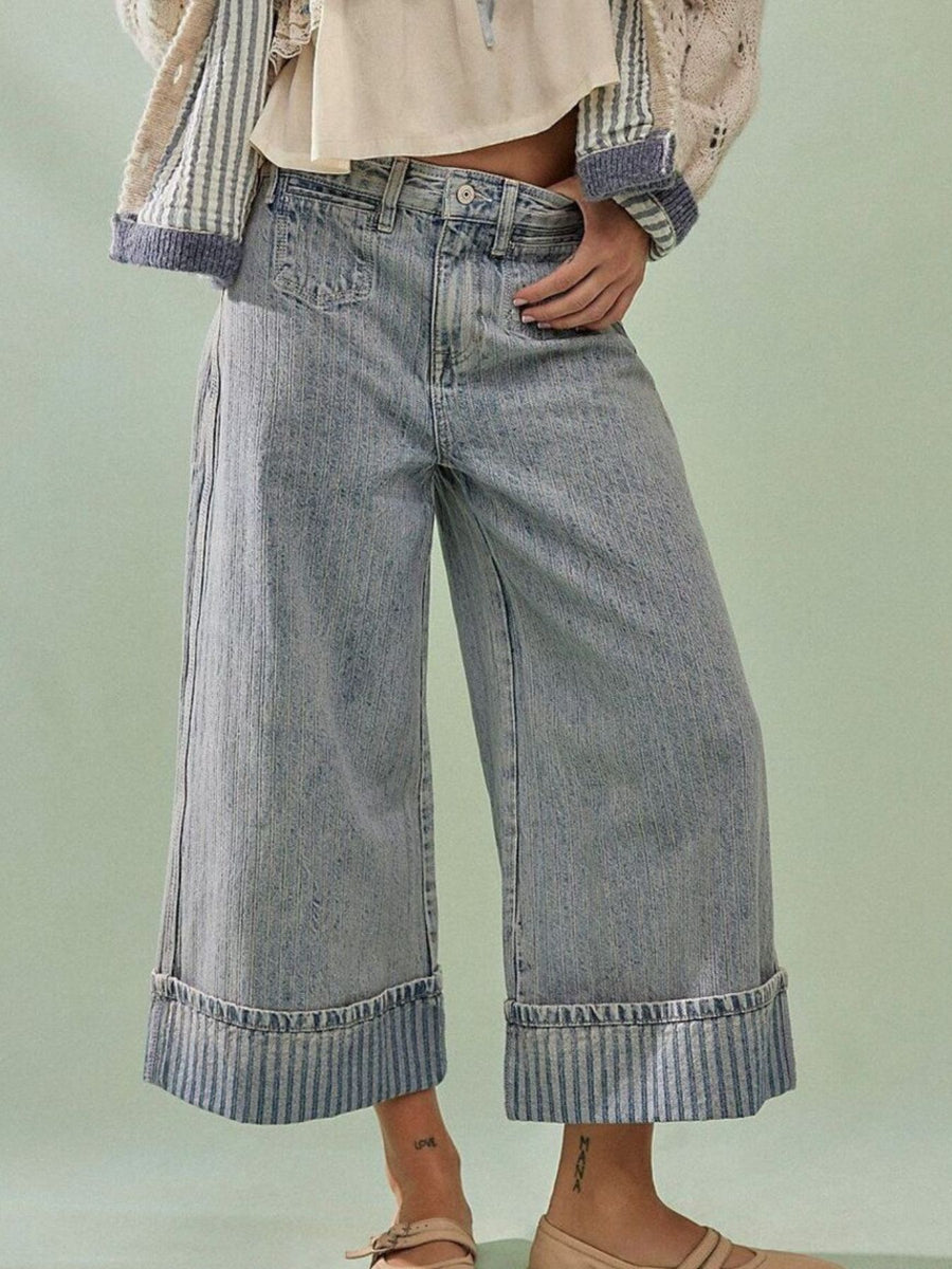 Person wearing wide-leg jeans and a striped shirt on a light green background