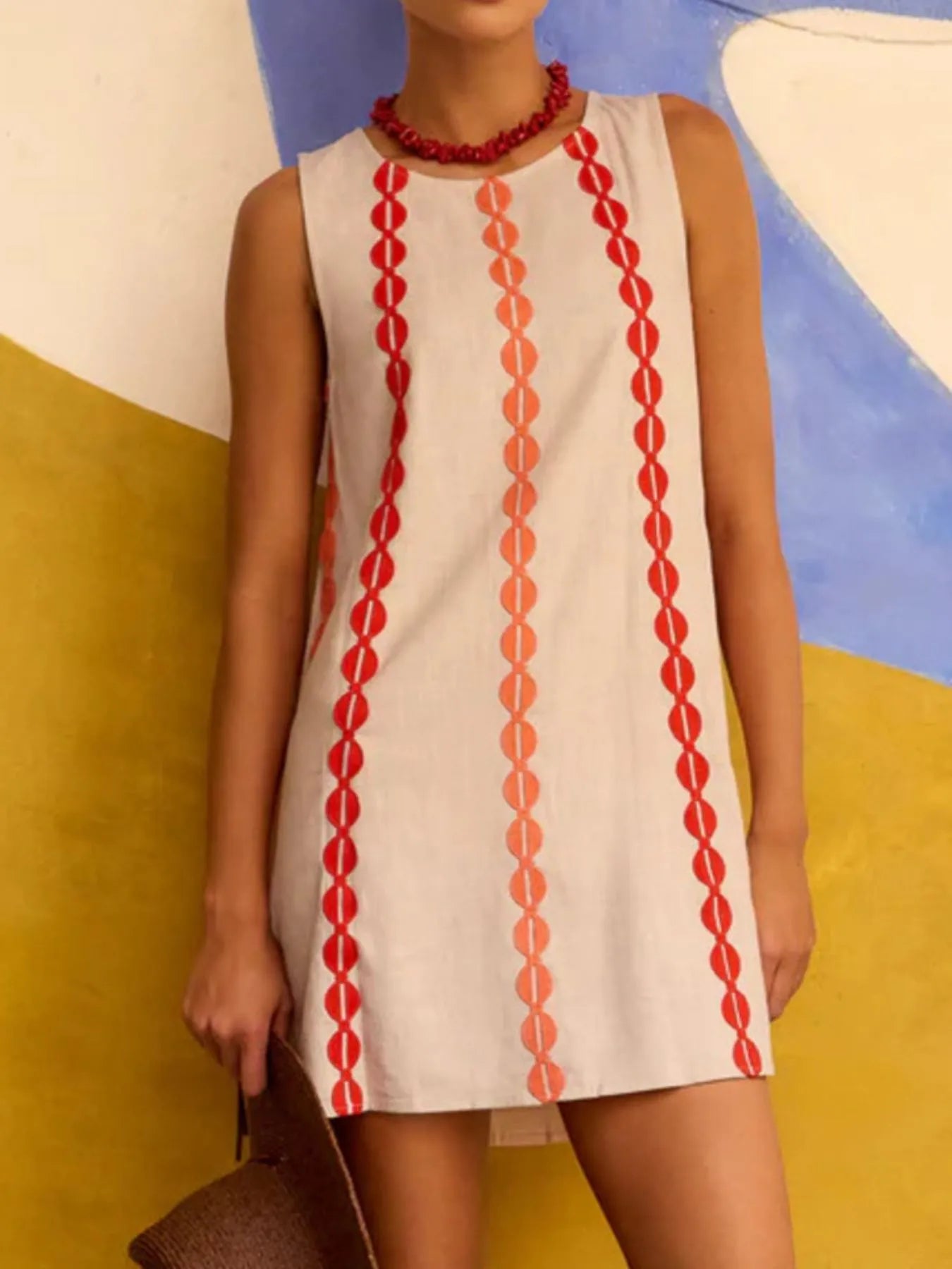 Woman wearing a sleeveless dress with red pattern against a colorful abstract background