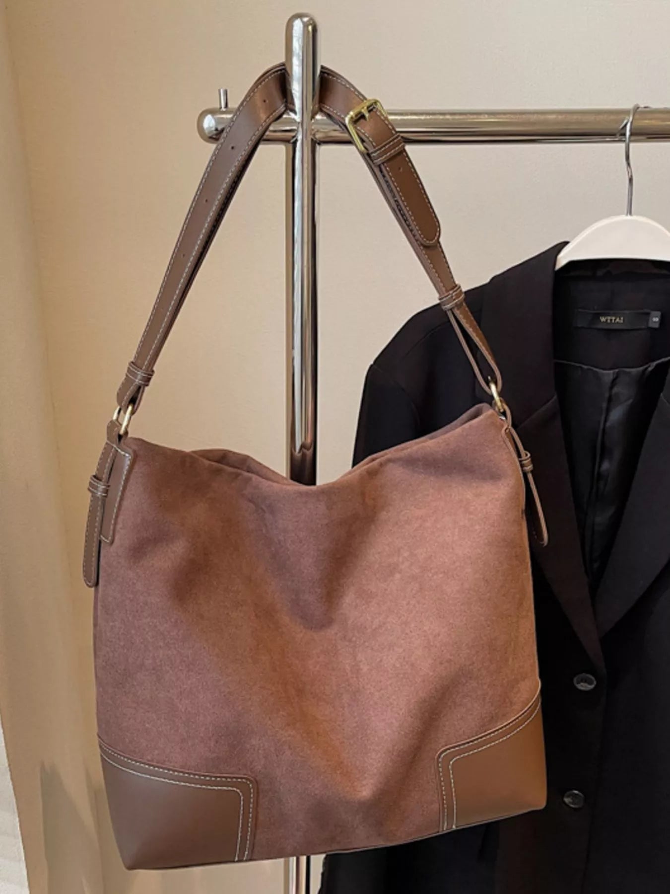 Brown leather handbag hanging on a rack with a coat in the background