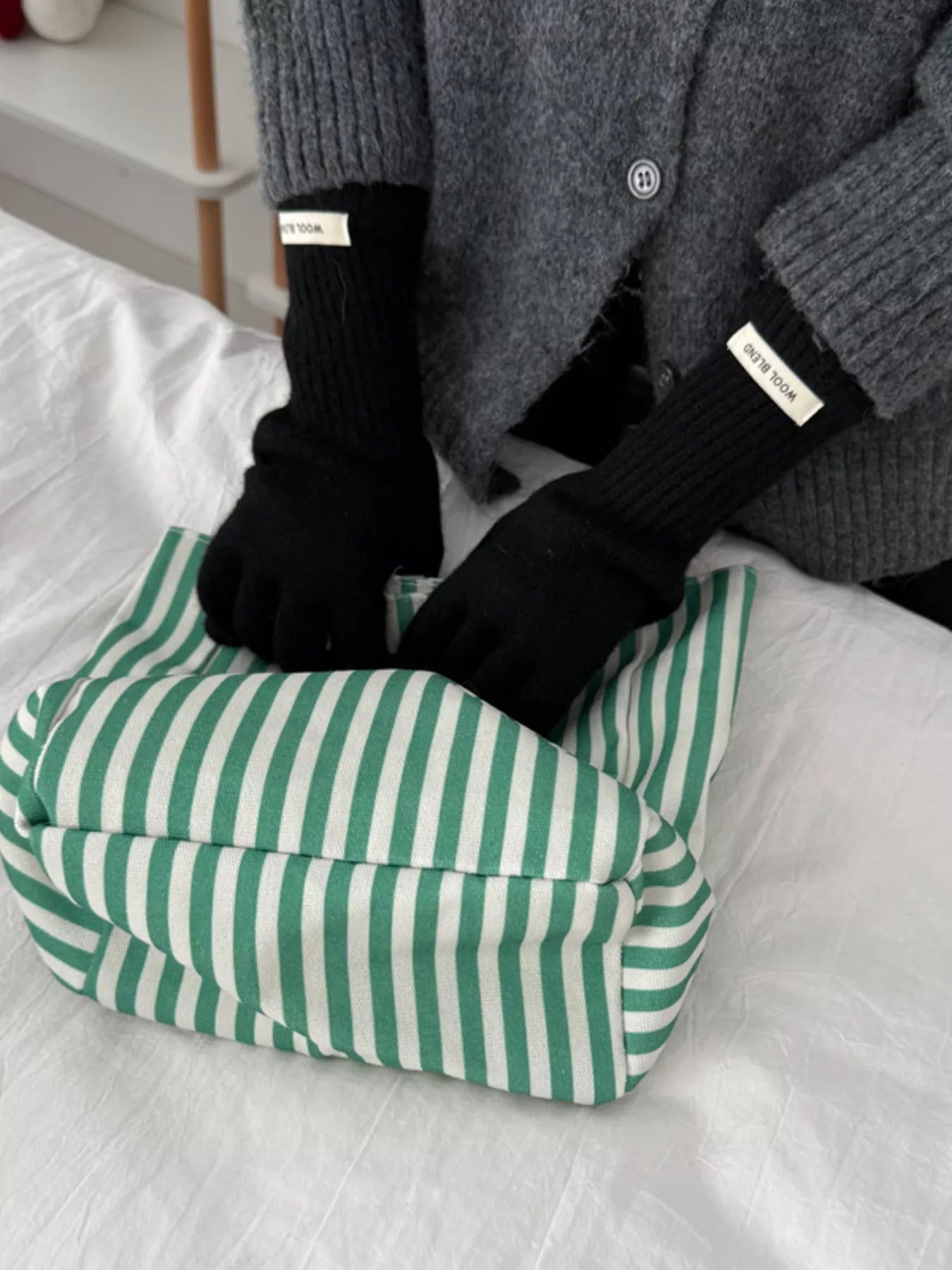 Person wearing black gloves with white labels on a green and white striped cushion.