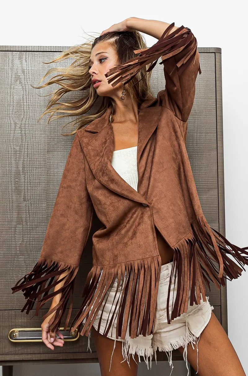 Woman wearing a brown suede fringe jacket in front of a textured wall.