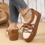 Brown and white sneakers with a fluffy interior worn by a person on a beige surface.
