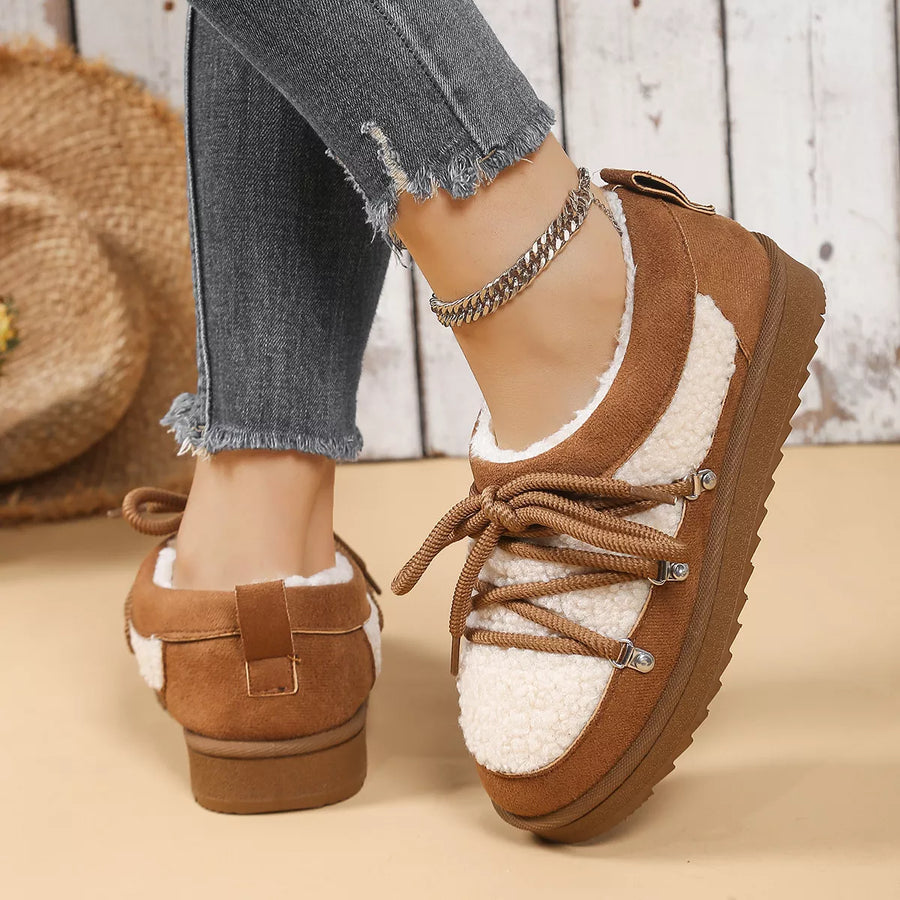 Brown and white sneakers with a fluffy interior worn by a person on a beige surface.