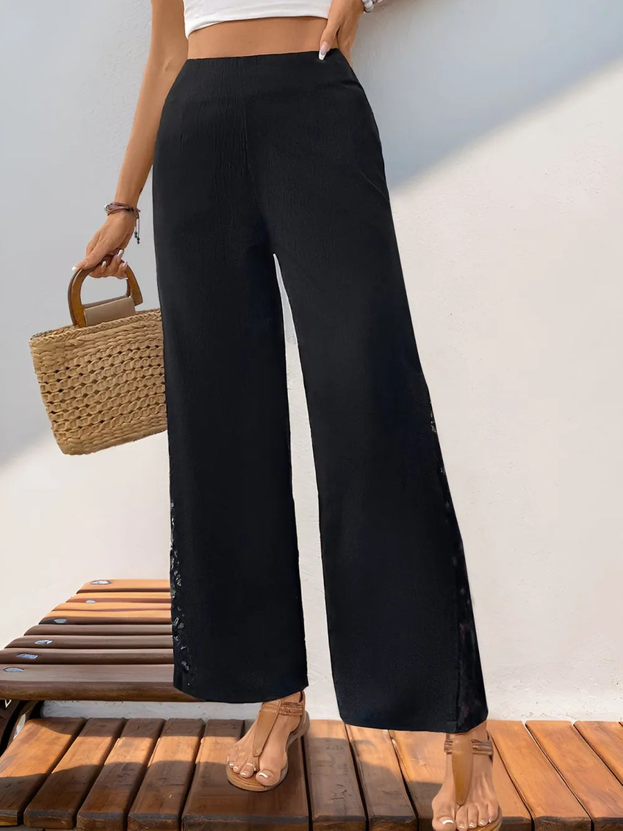 Person wearing black wide-leg pants and a white crop top, standing on a wooden deck.