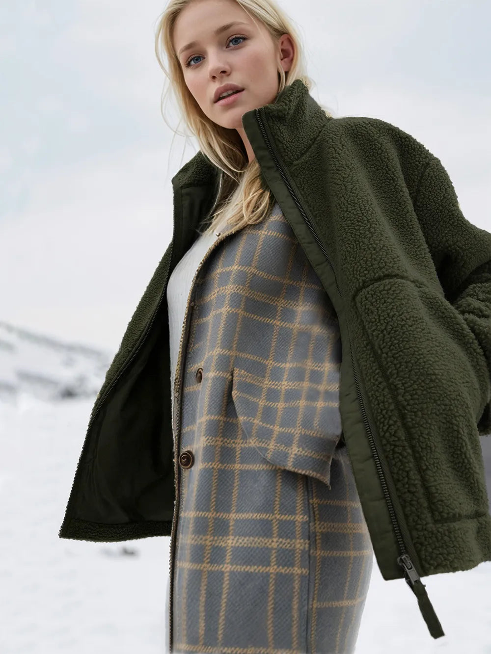 Woman wearing a green coat over a plaid outfit in a snowy landscape