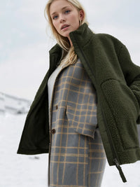 Woman wearing a green coat over a plaid outfit in a snowy landscape
