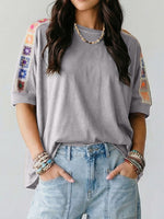 Person wearing a gray t-shirt with colorful sleeve designs and light blue jeans on a plain background