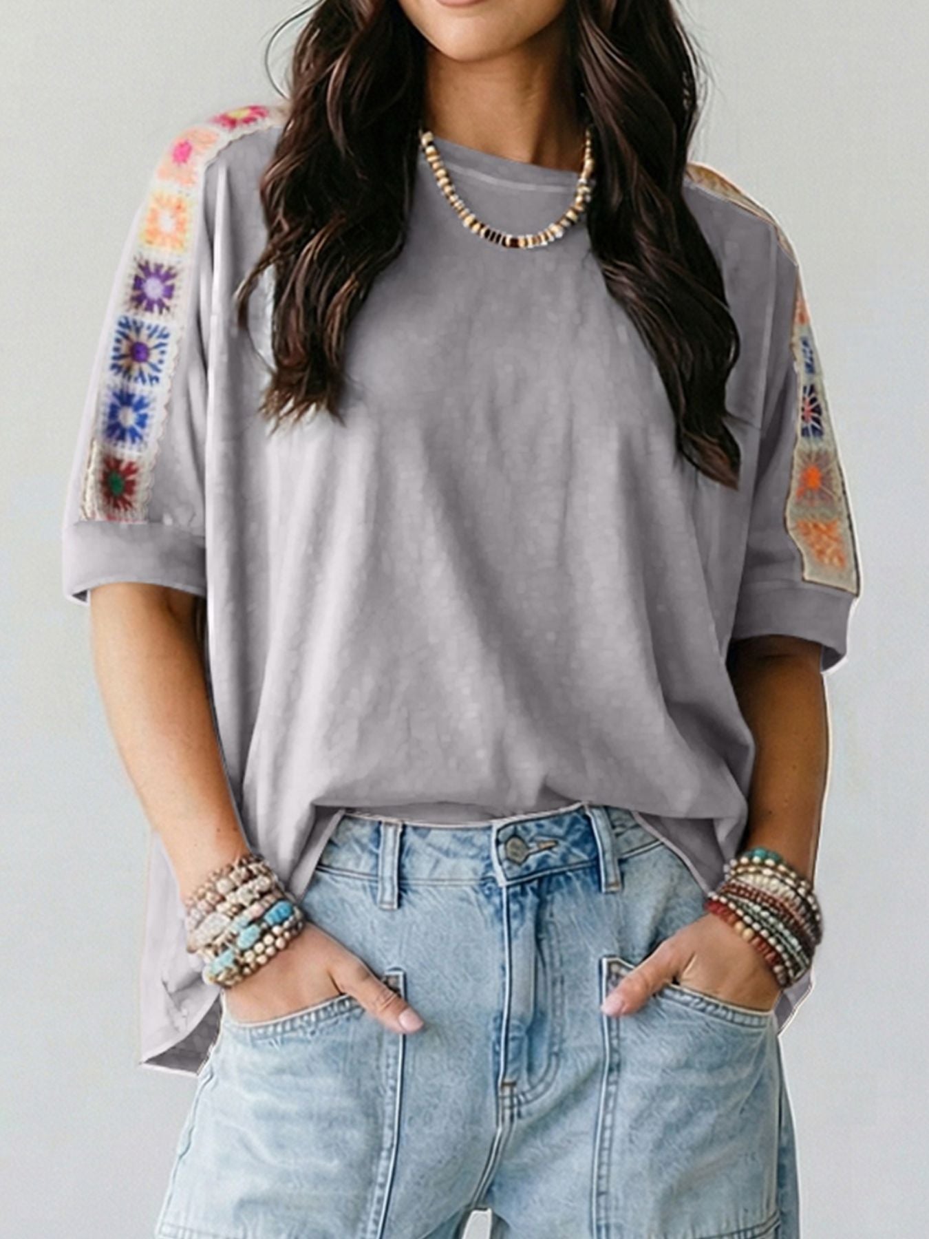 Person wearing a gray t-shirt with colorful sleeve designs and light blue jeans on a plain background