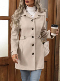 Woman wearing a beige coat with black buttons, holding a coffee cup, standing in front of a wooden door.